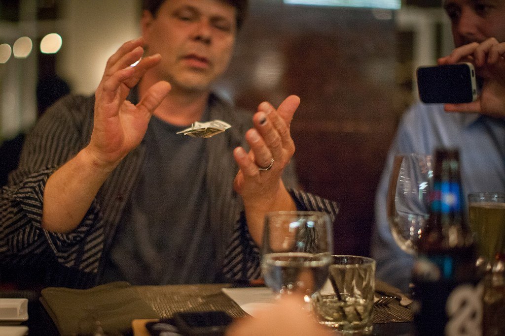 Rob Fore performing a close-up money trick at a table while a guest films it